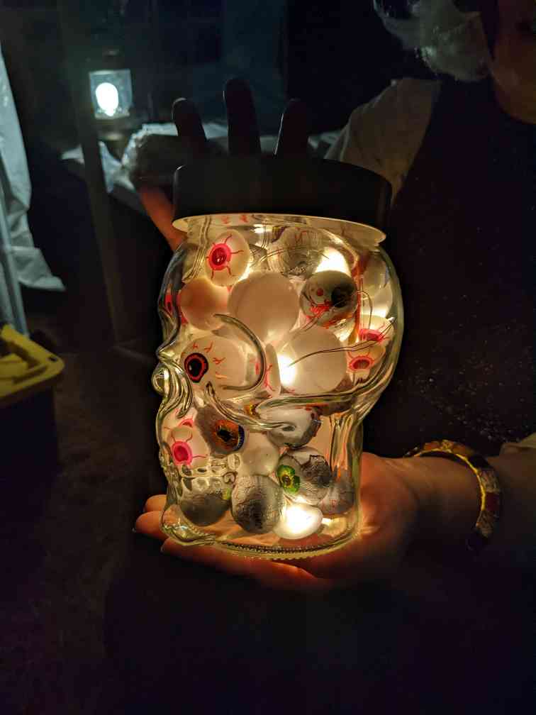 A jar of glowing eyeballs held in someone's hands.